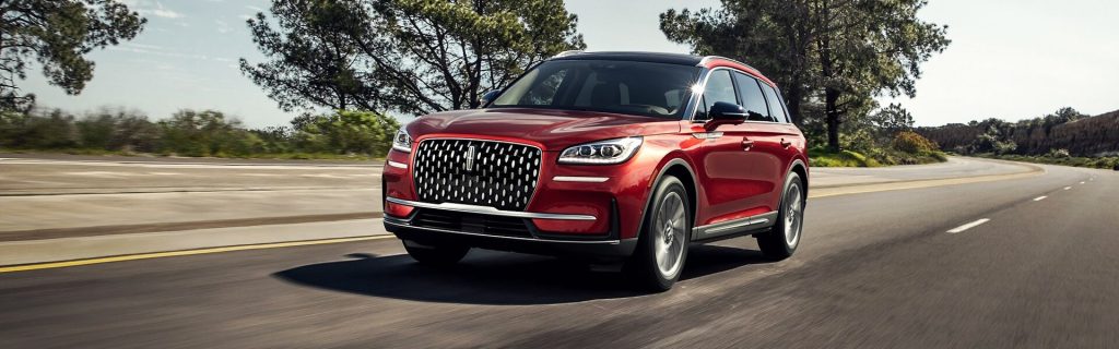 A red 2024 Lincoln Corsair driving along a scenic road near London, KY, showcasing its elegant design and smooth performance.