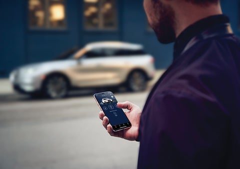 A person is shown interacting with a smartphone to connect to a Lincoln vehicle across the street. | Don Franklin Lincoln in London KY