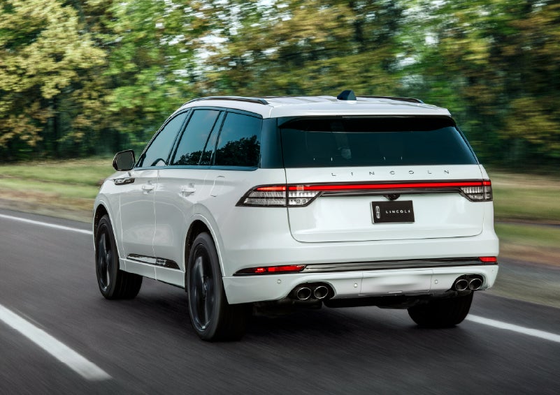 A white 2026 Lincoln Aviator® SUV is being driven away down a road lined with colorful trees. | Don Franklin Lincoln in London KY