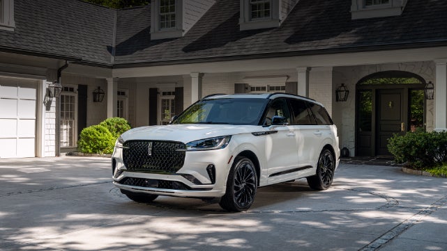A white 2026 Lincoln Aviator® SUV is parked in the driveway of a luxury home. | Don Franklin Lincoln in London KY