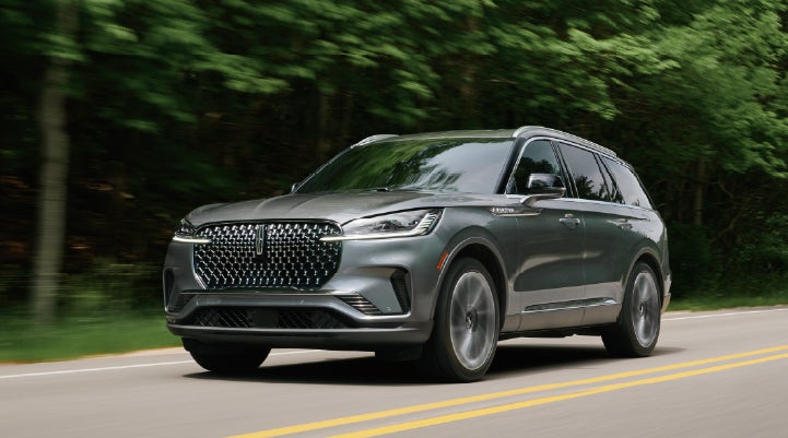 A 2027 Lincoln Aviator® SUV is being driven down a road lined with trees. | Don Franklin Lincoln in London KY